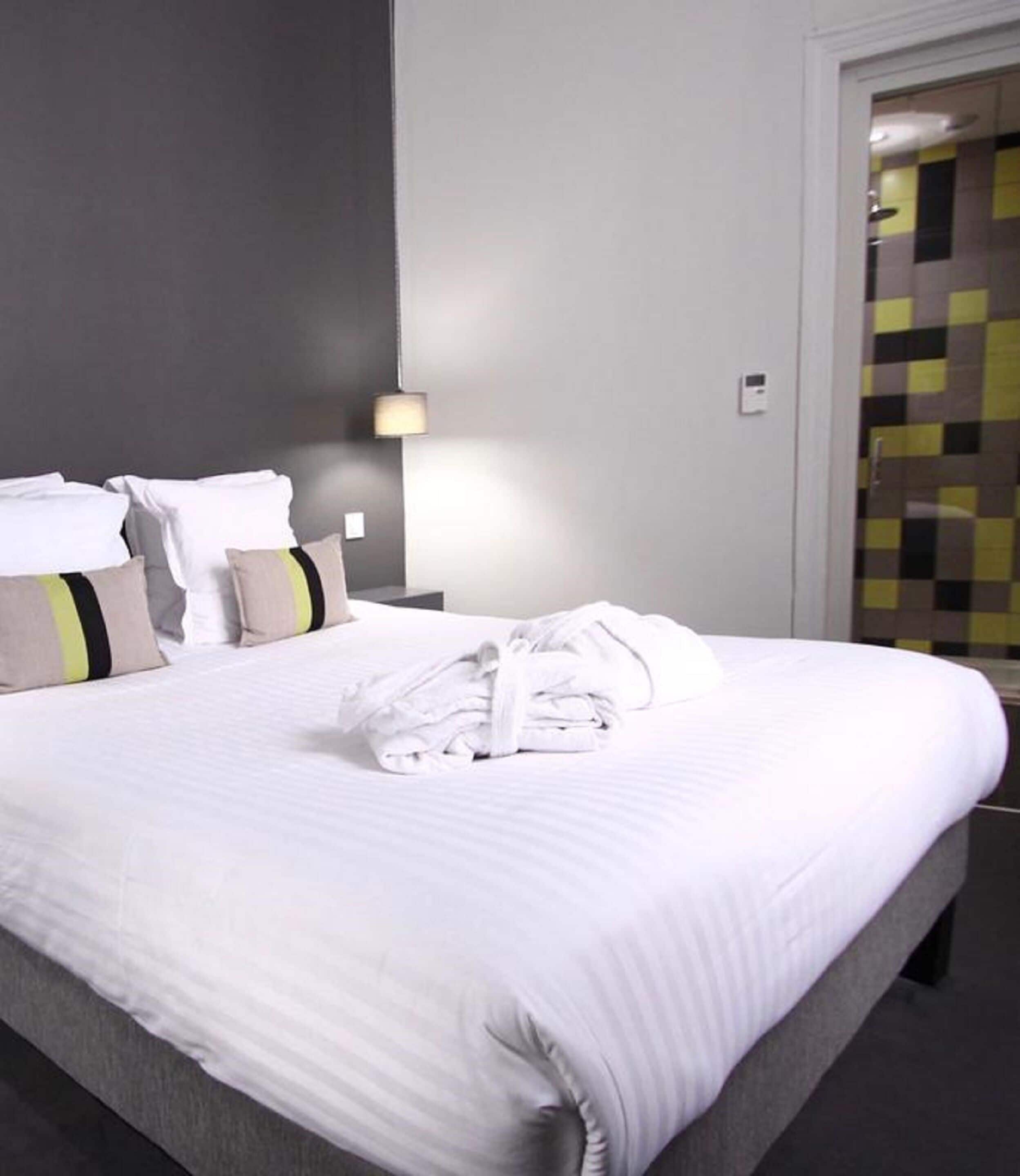 A neatly made bed with white linens and a folded towel, a bedside lamp, and a wall with a checkered pattern.