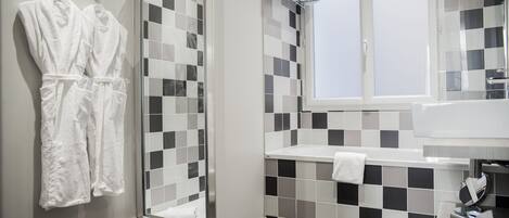 A modern bathroom with a checkered tile backsplash, a glass shower enclosure, and a white sink with a towel on the counter.