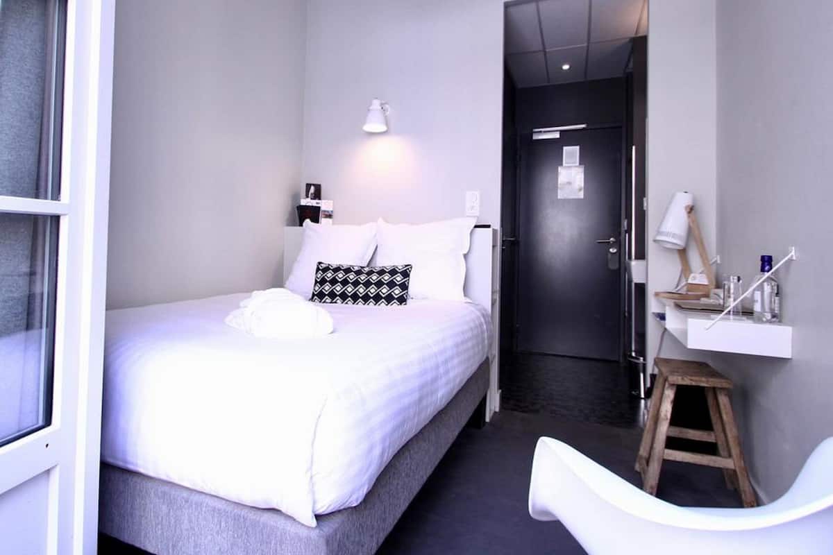 Quarto de hotel moderno com cama, mesa de cabeceira e um pequeno banquinho.
