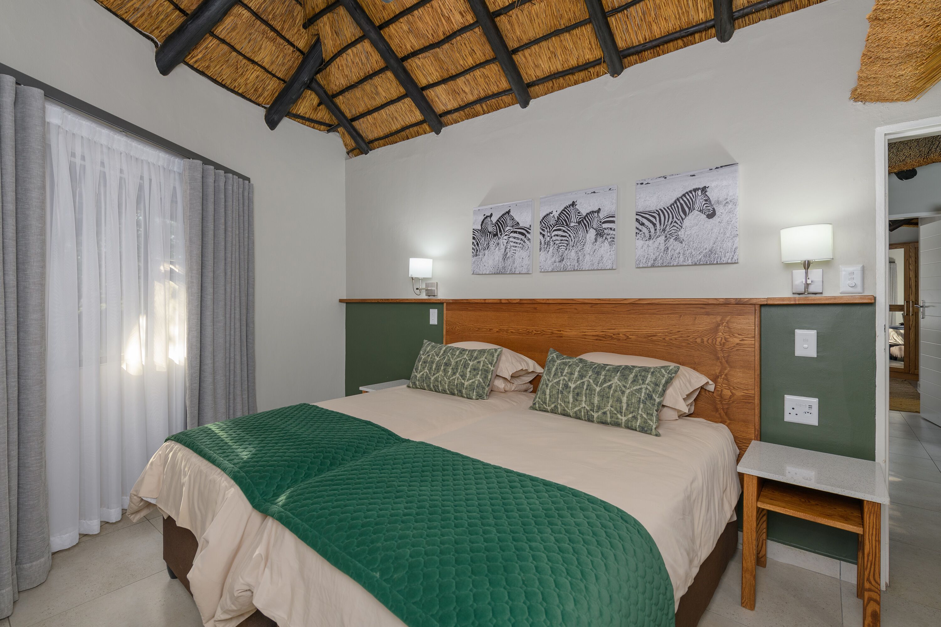 Ein Schlafzimmer mit einem Bett, zwei Kissen, einer grünen Decke, einem Nachttisch, einer Lampe und einem Wandbild mit Zebra-Motiv.