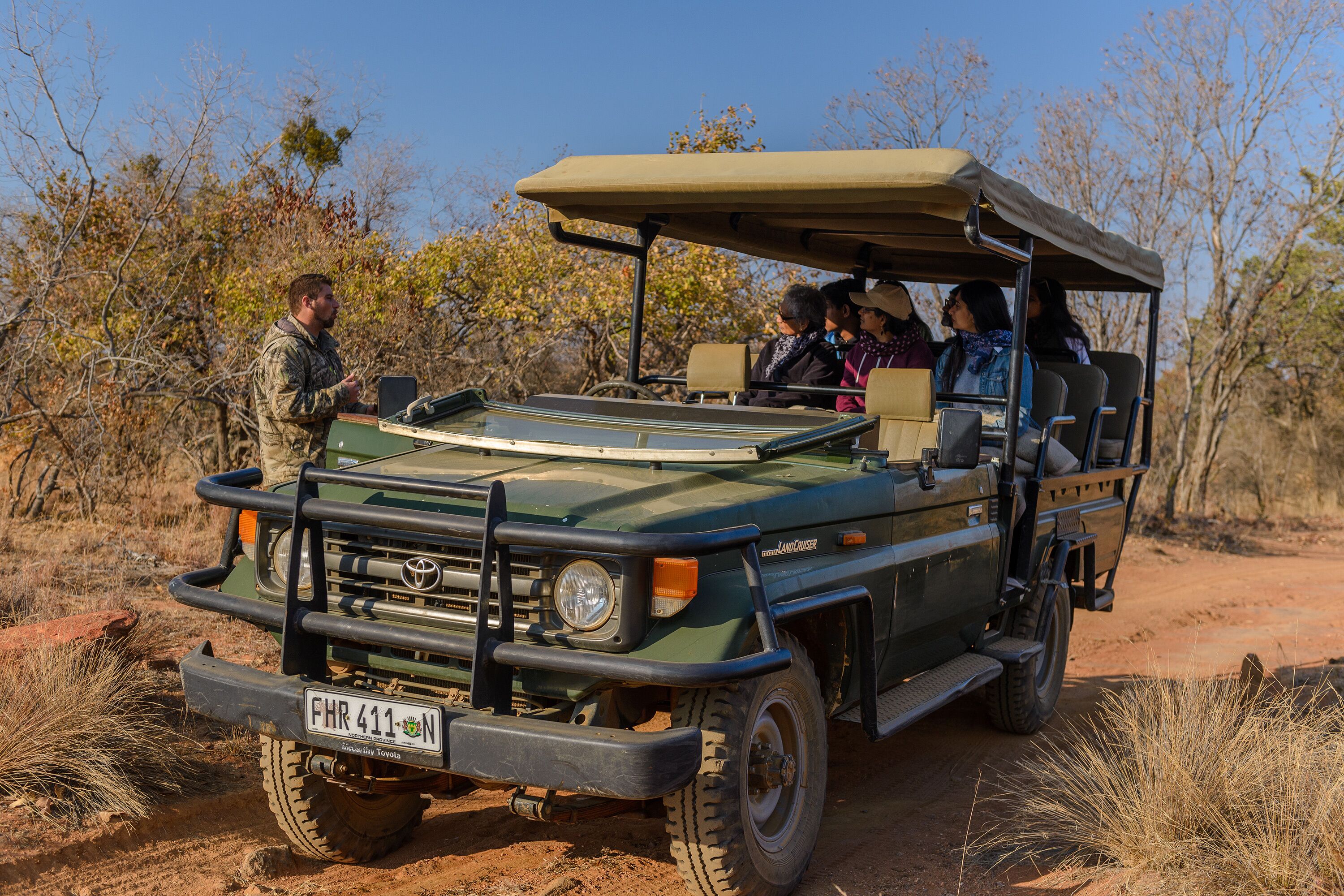 A safari vehicle with a roof, passengers, and a guide standing outside.