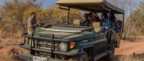 A safari vehicle with a roof, passengers, and a guide standing outside.