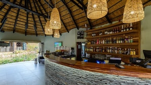 A bar area with a stone counter, wooden shelves with bottles, and hanging wicker lamps. - Waterberg Game Park (Vaalwater)
