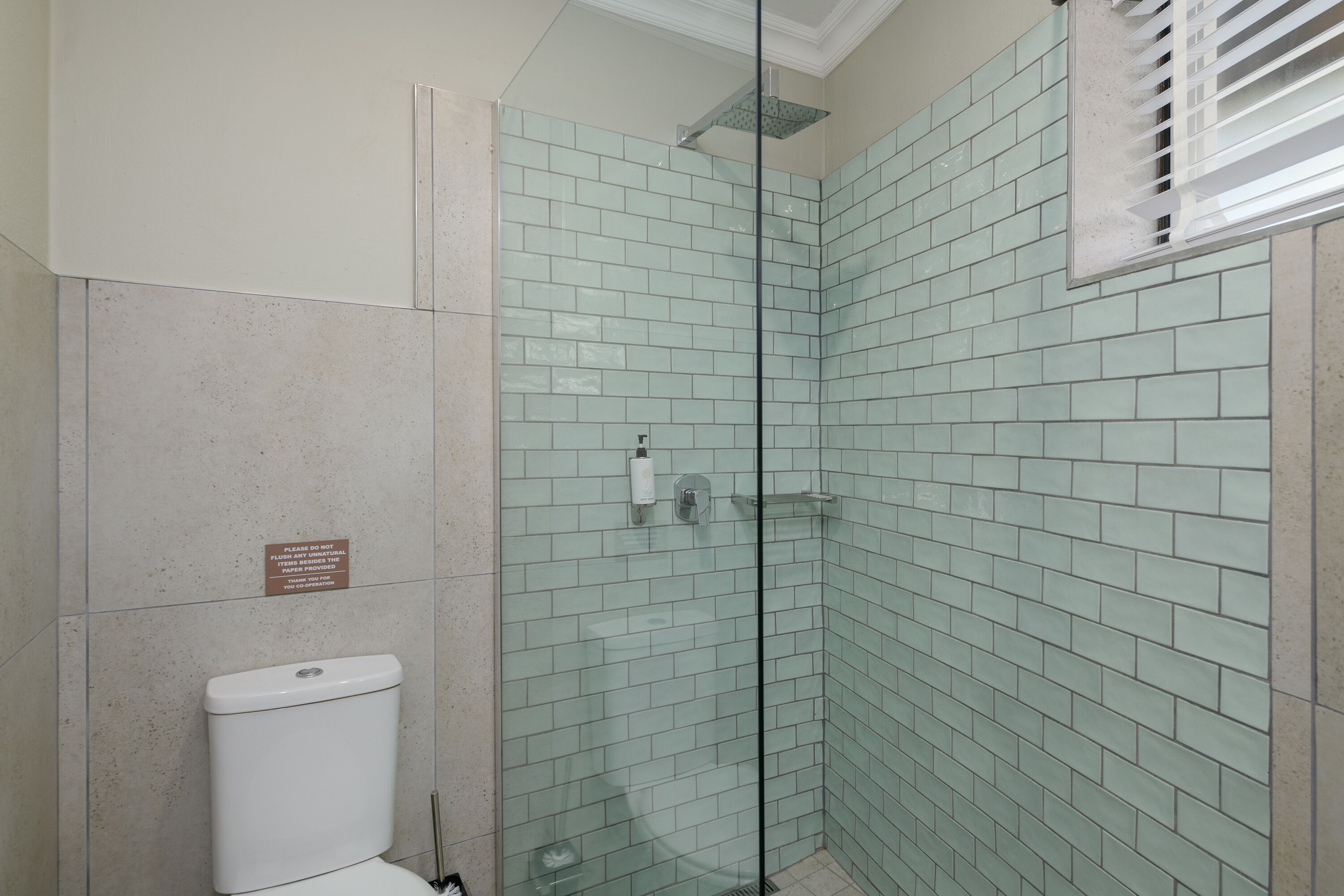 Un baño con ducha de vidrio, paredes de azulejos y un inodoro.