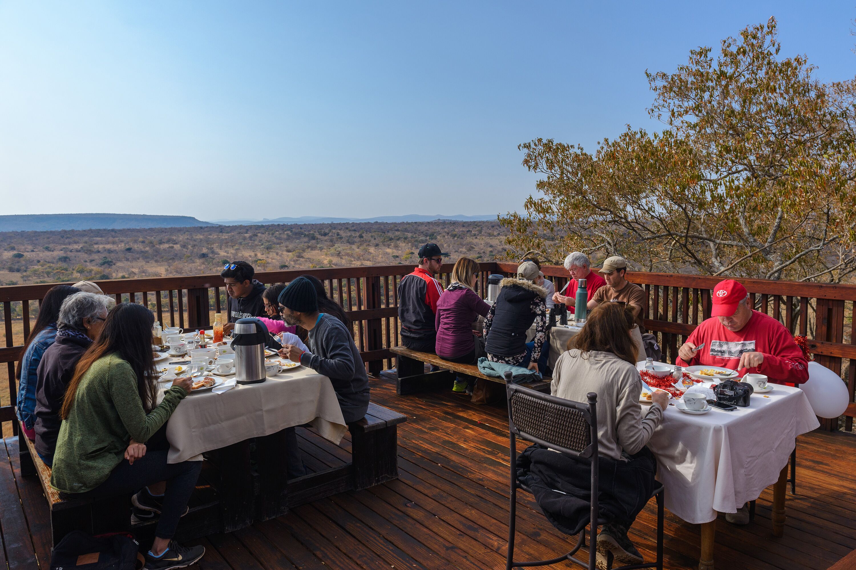 A group of people dining outdoors on a wooden deck with tables set up for meals.