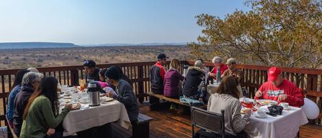 A group of people dining outdoors on a wooden deck with tables set up for meals.