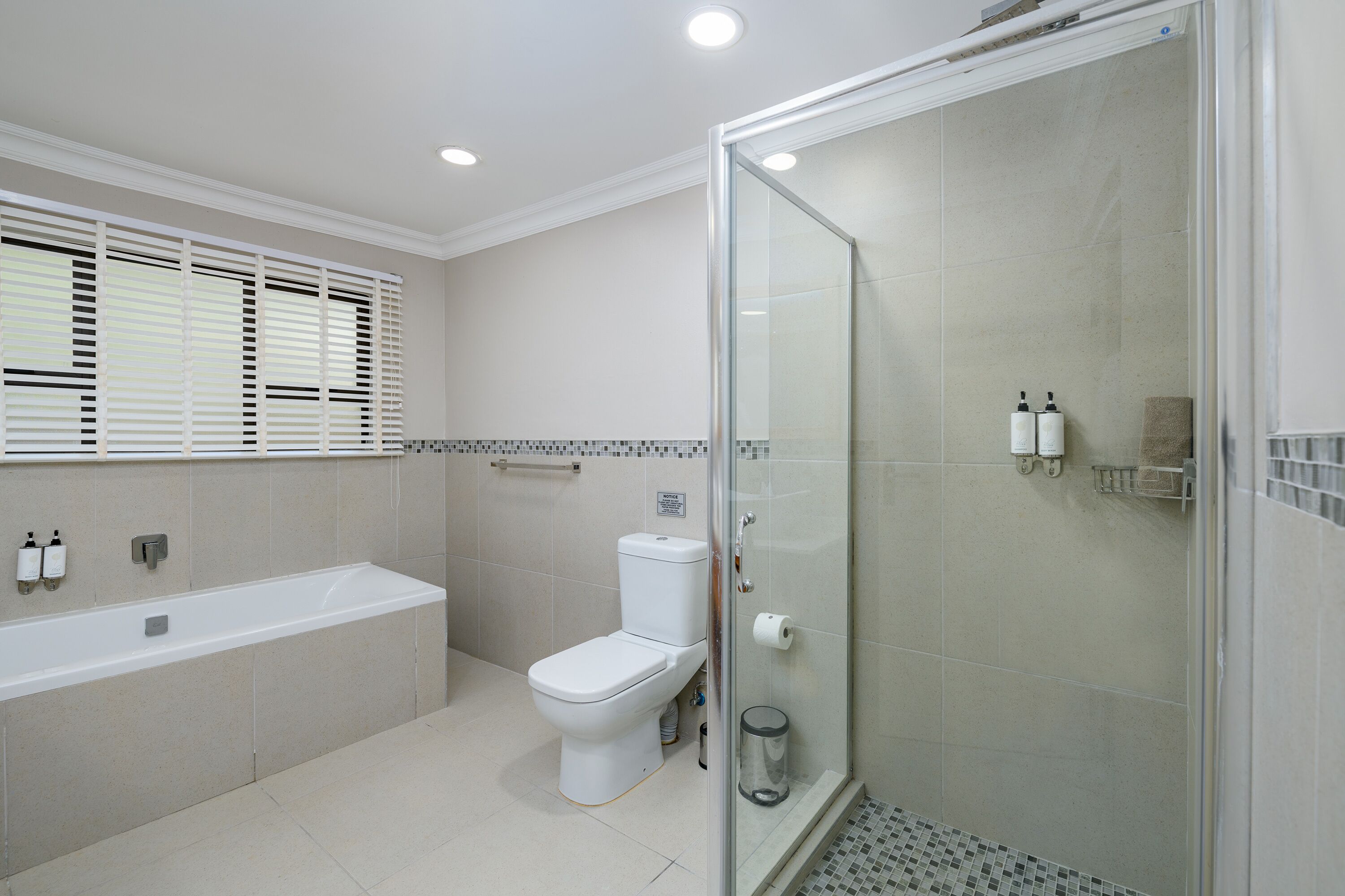 A modern bathroom with a glass-enclosed shower, a white bathtub, and a toilet.