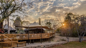 A wooden deck with a stone wall, a covered area with a canopy, and a sunset in the background. - Waterberg Game Park (Vaalwater)