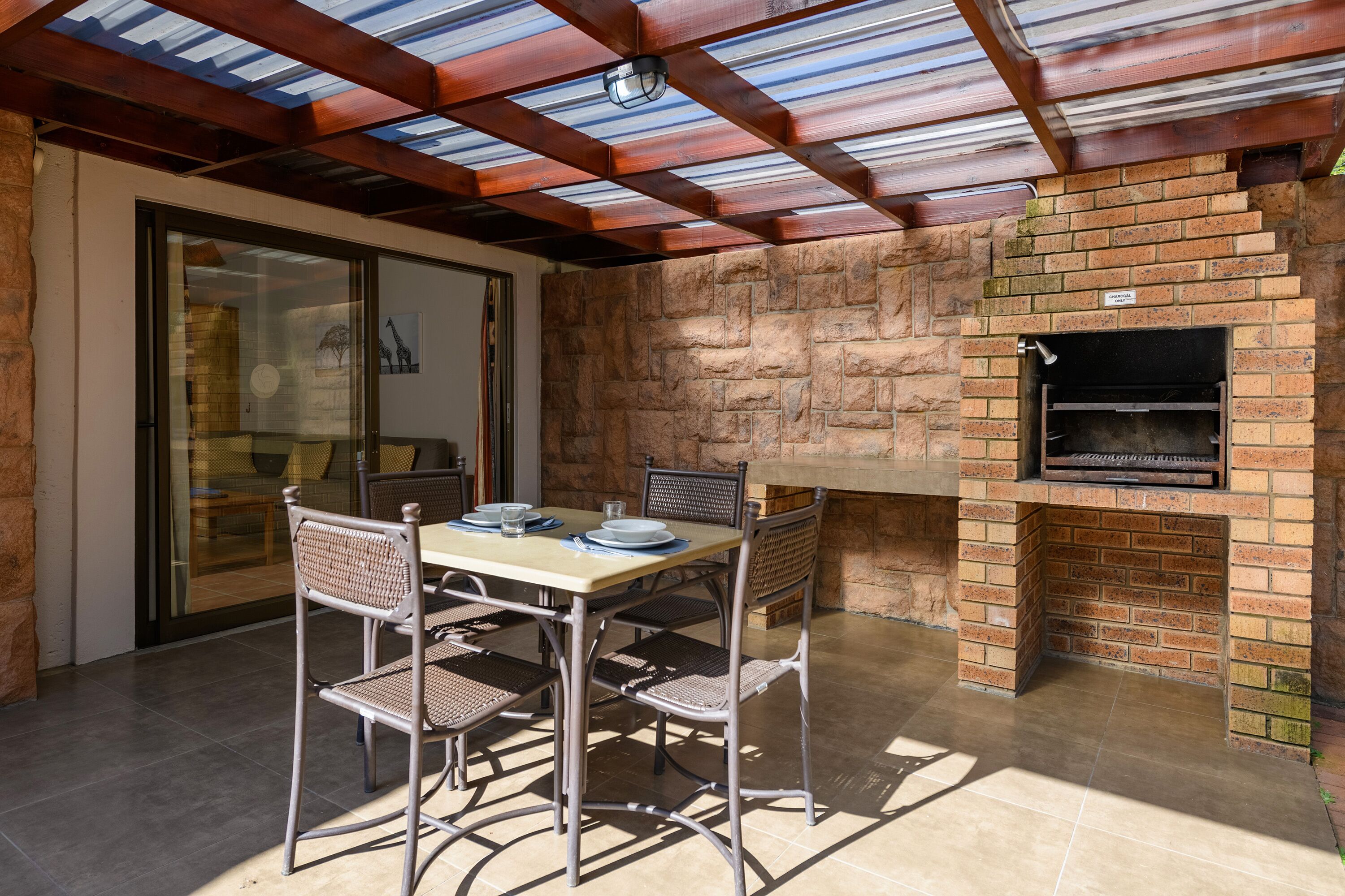 An outdoor patio with a brick fireplace, a table set for dining, and a covered area with a skylight.