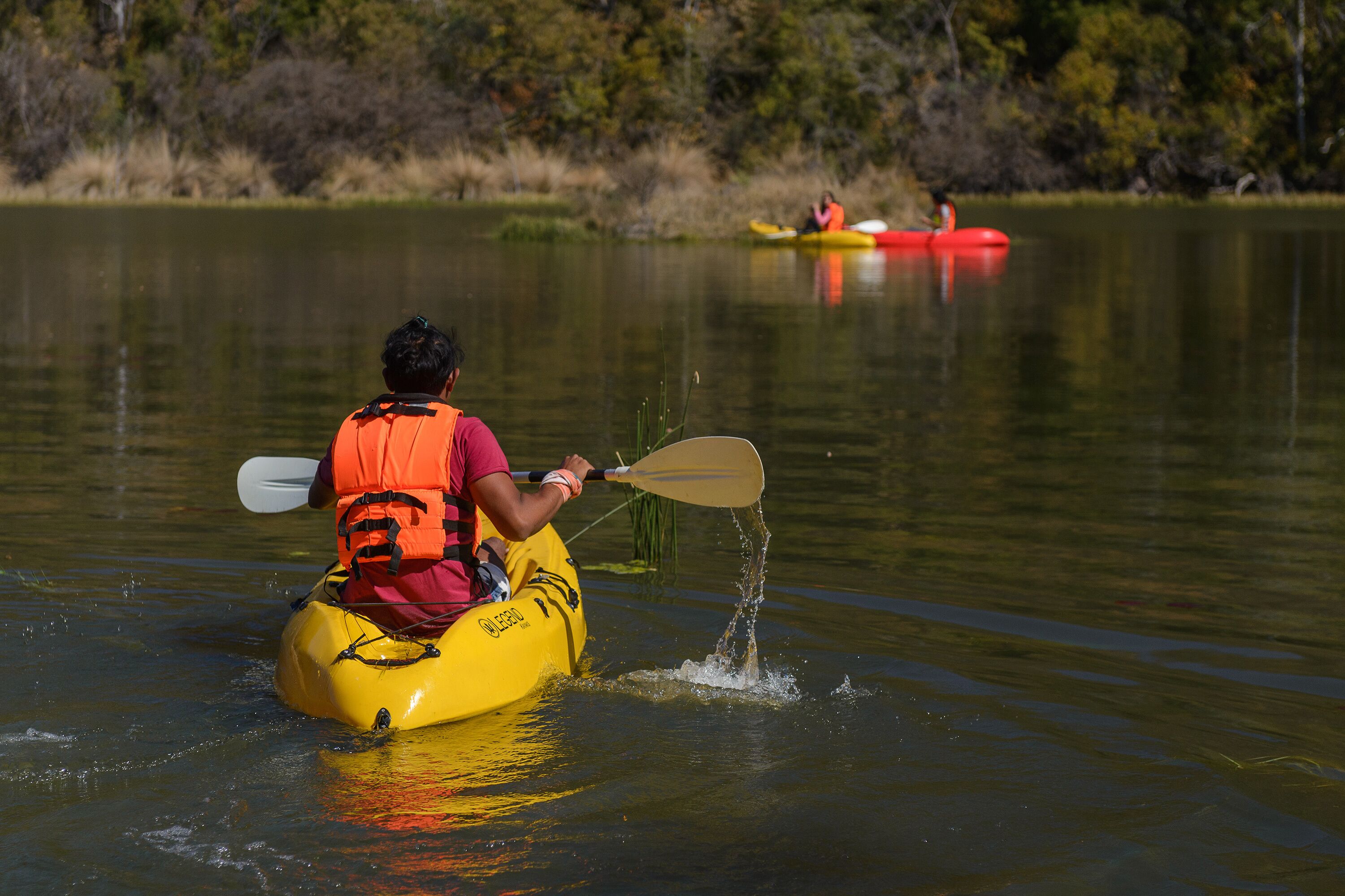 A person kayaking on a calm lake with another kayak in the background.