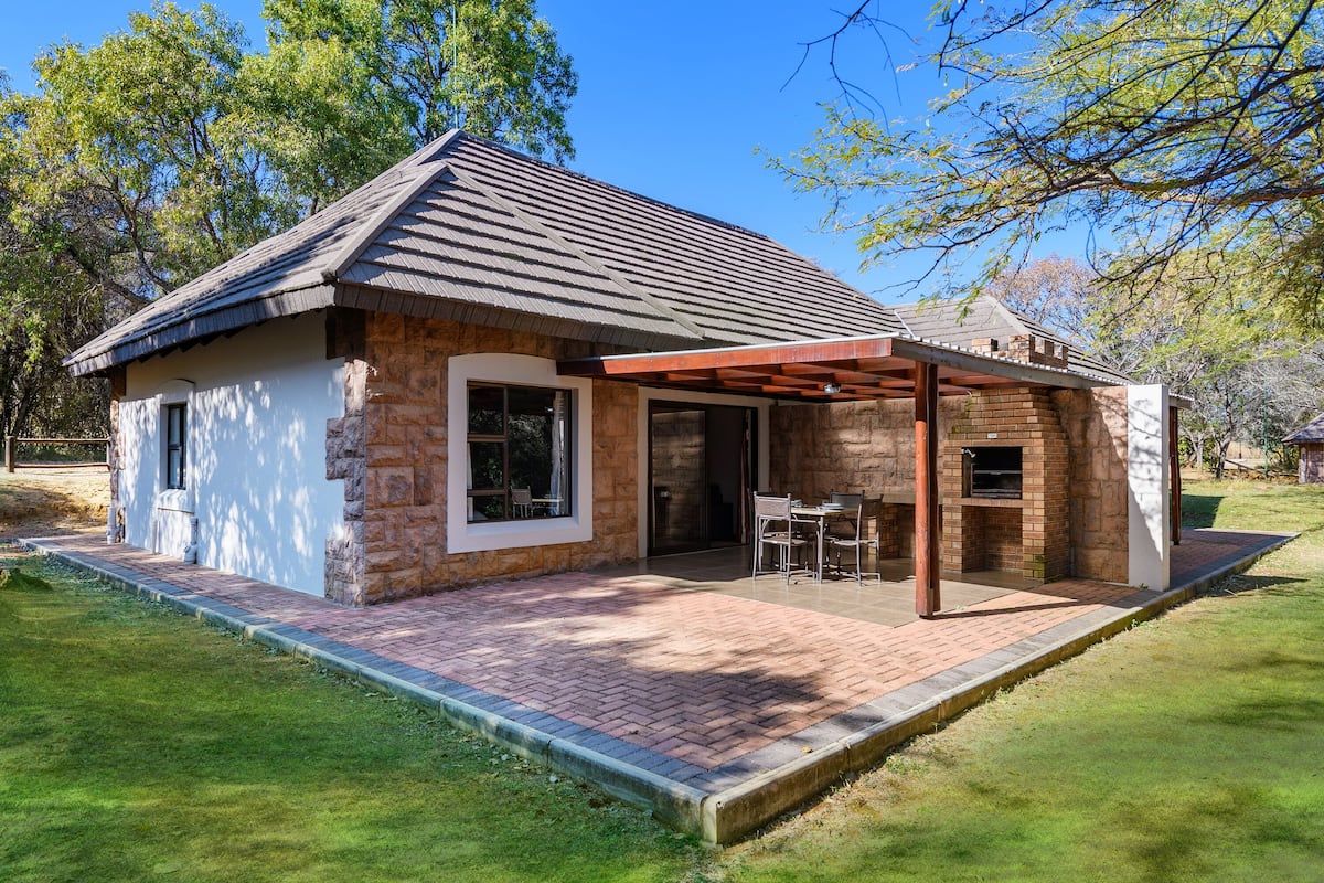A small stone house with a brick patio, a covered outdoor seating area, and a brick fireplace.