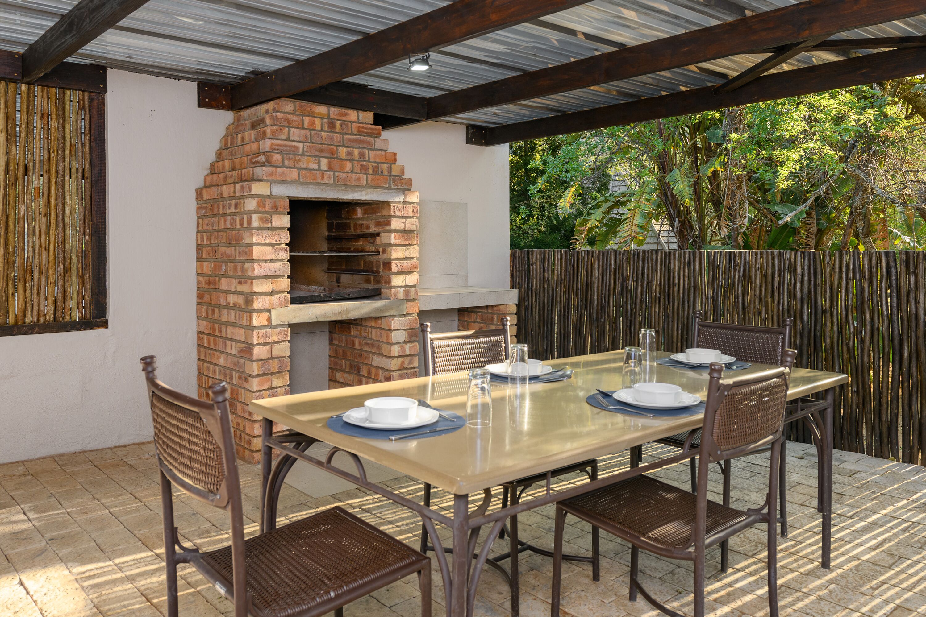 An outdoor patio with a brick oven, a table set for four, and wicker chairs.