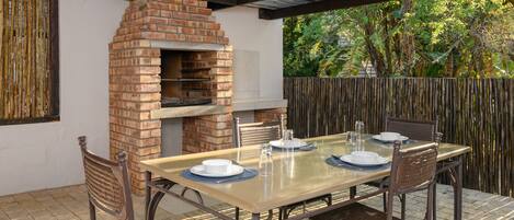 An outdoor patio with a brick oven, a table set for four, and wicker chairs.