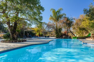 A swimming pool with tiled edges, surrounded by lounge chairs and a shaded area.