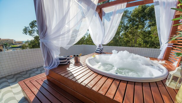 A wooden deck with a hot tub, white curtains, and a tiled wall. - Mar e Mar Florianópolis (Florianópolis)