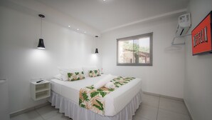 A bedroom with a bed, bedside tables, a hanging light, a window with blinds, and a wall-mounted air conditioner. - Mar e Mar Florianópolis (Florianópolis)