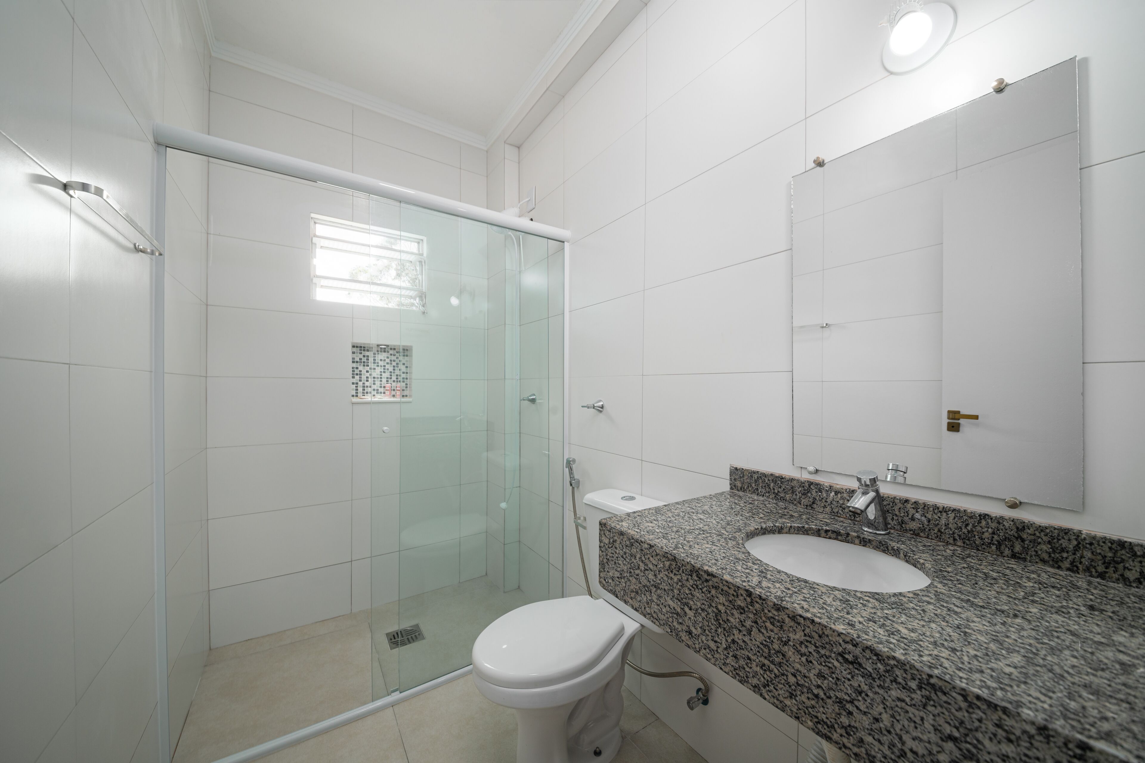 Un baño moderno con cabina de ducha de vidrio, inodoro blanco, lavamanos con encimera de granito y un espejo grande.