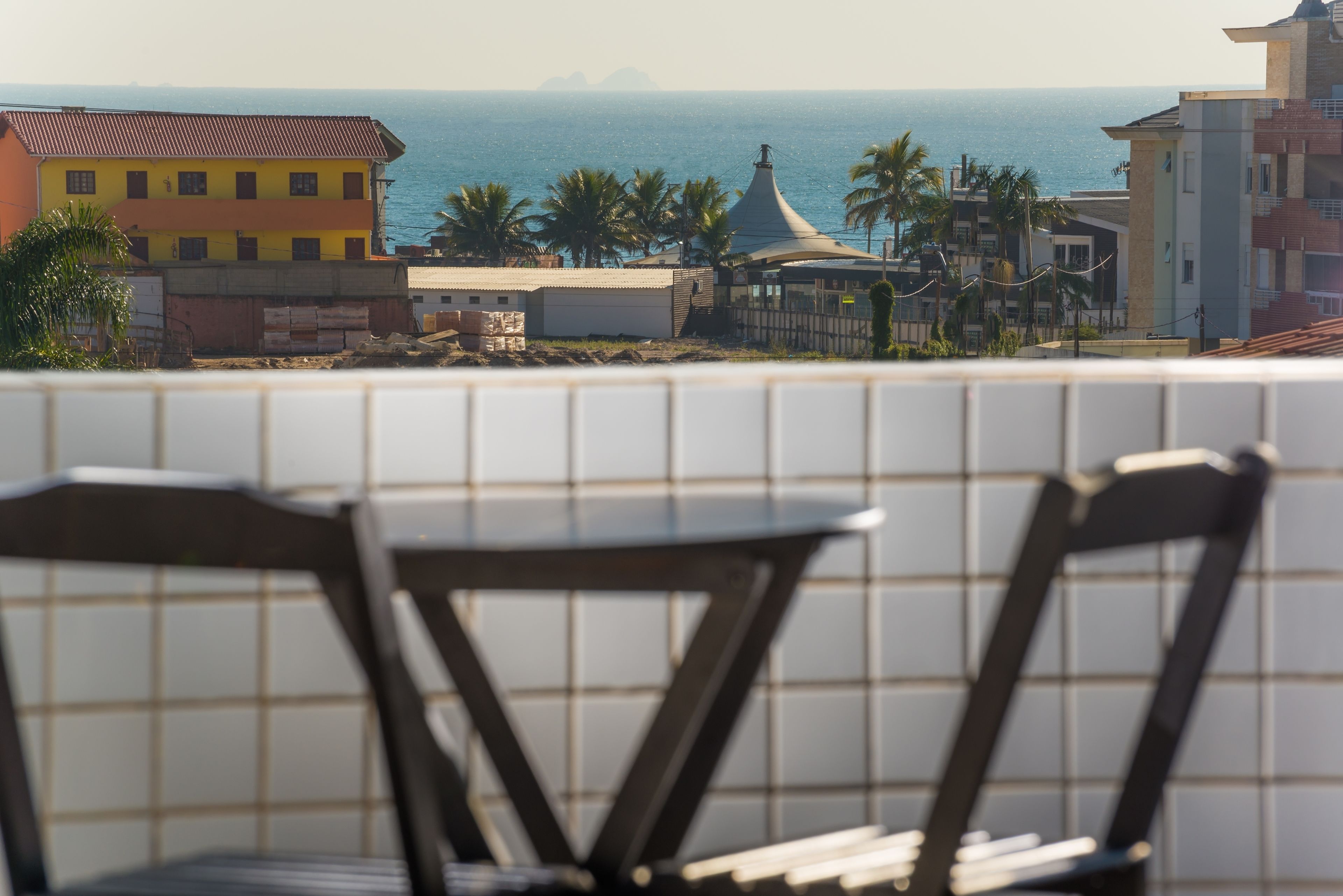 A view of a coastal area with a dining area featuring two chairs and a table, overlooking the sea and palm trees.