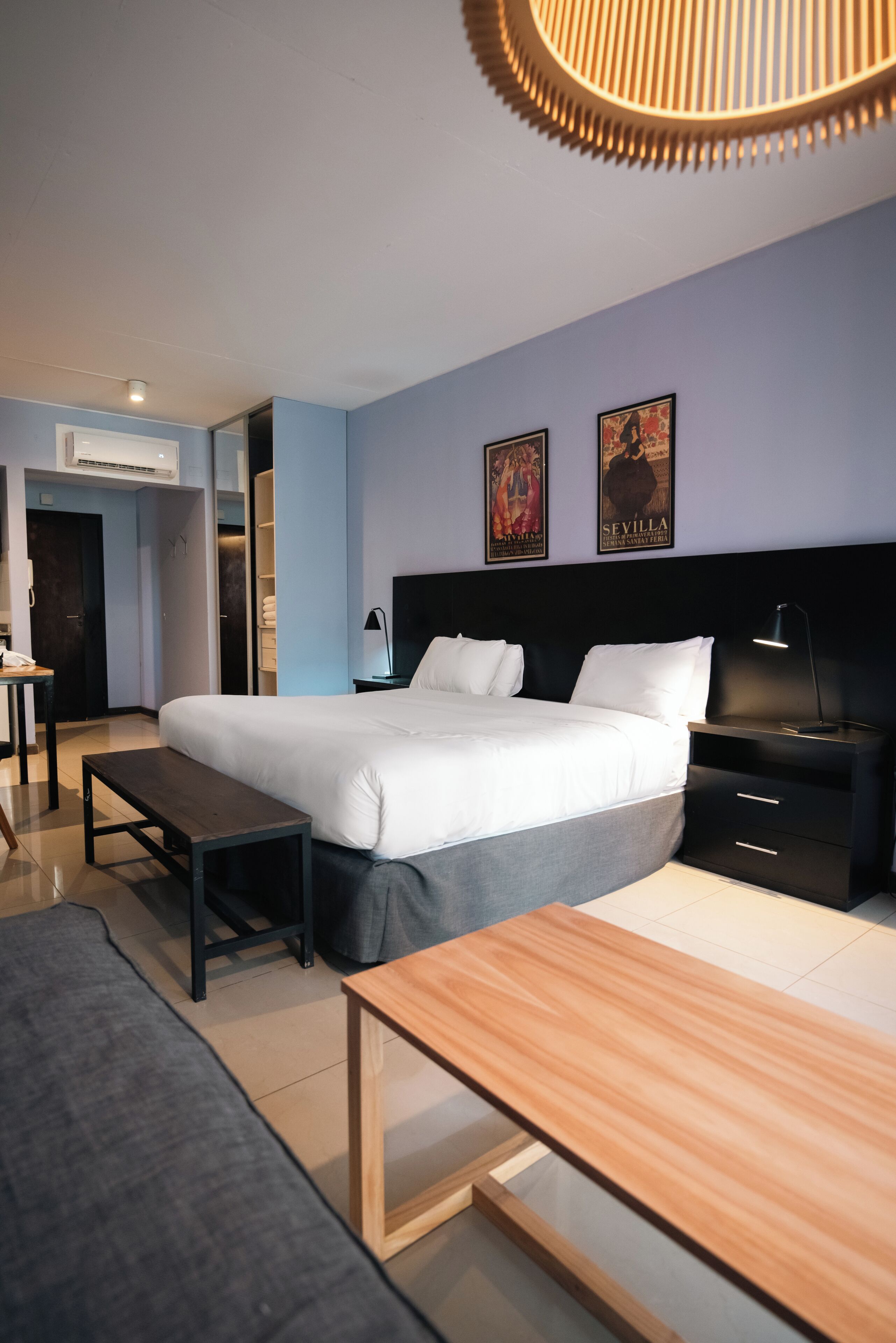 Una habitación de hotel moderna con una cama grande, mesitas de noche, un escritorio y una lámpara colgante.