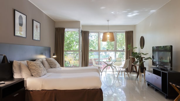 A modern hotel room with a large bed, a desk, a TV, and a dining area with a glass table and chairs. - Feel Buenos Aires (Buenos Aires)