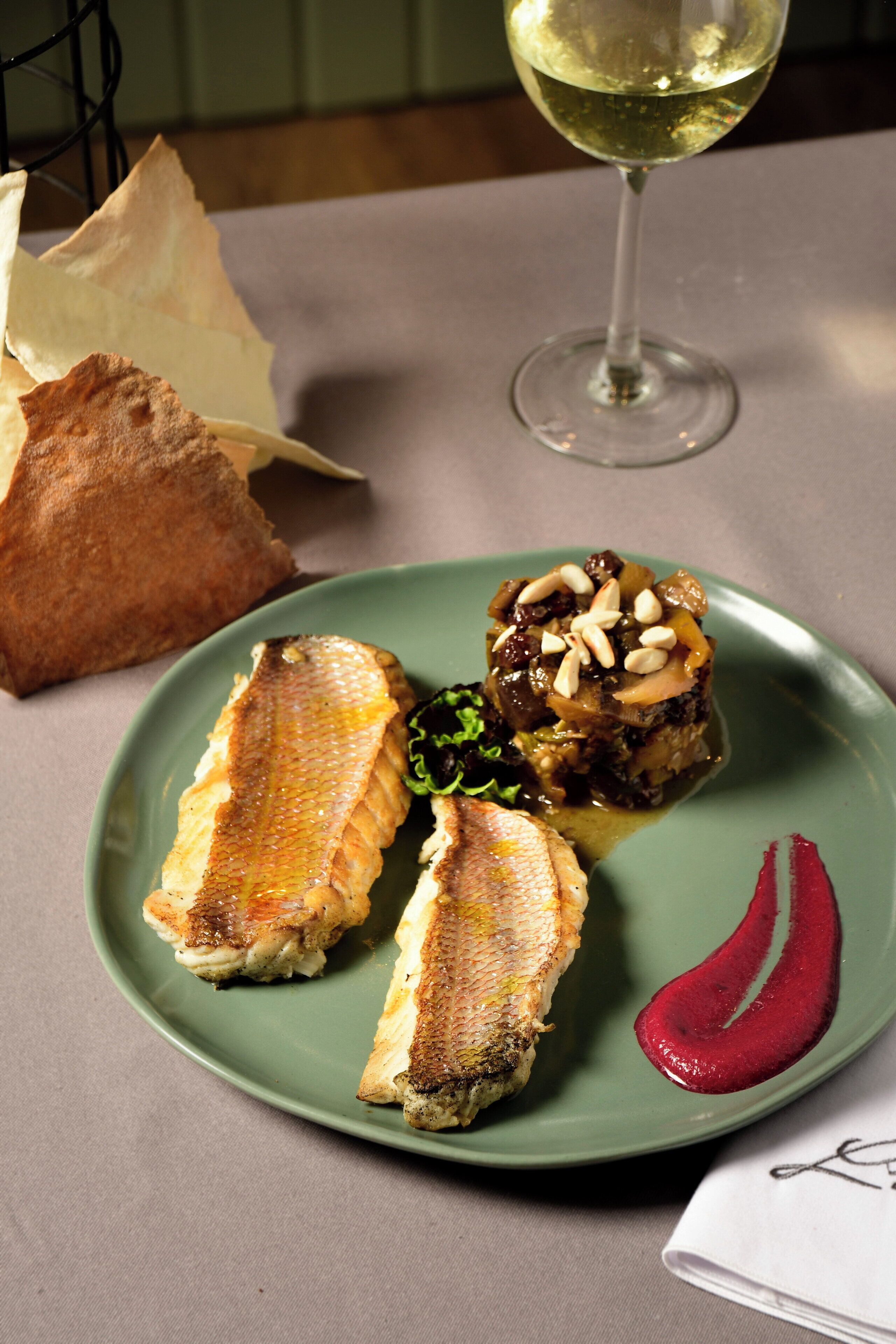 A plate of food with fish and a glass of white wine.