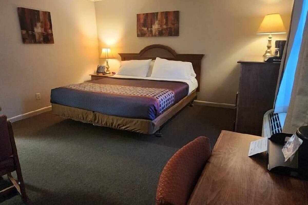 A hotel room with a bed, a desk, a chair, and two wall-mounted lamps.