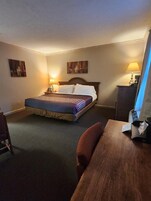 Una habitación de hotel con cama, escritorio, silla y dos lámparas fijadas a la pared.