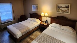 Hotelkamer met twee bedden, een raam met gordijnen, een wandlamp en twee ingelijste foto's.