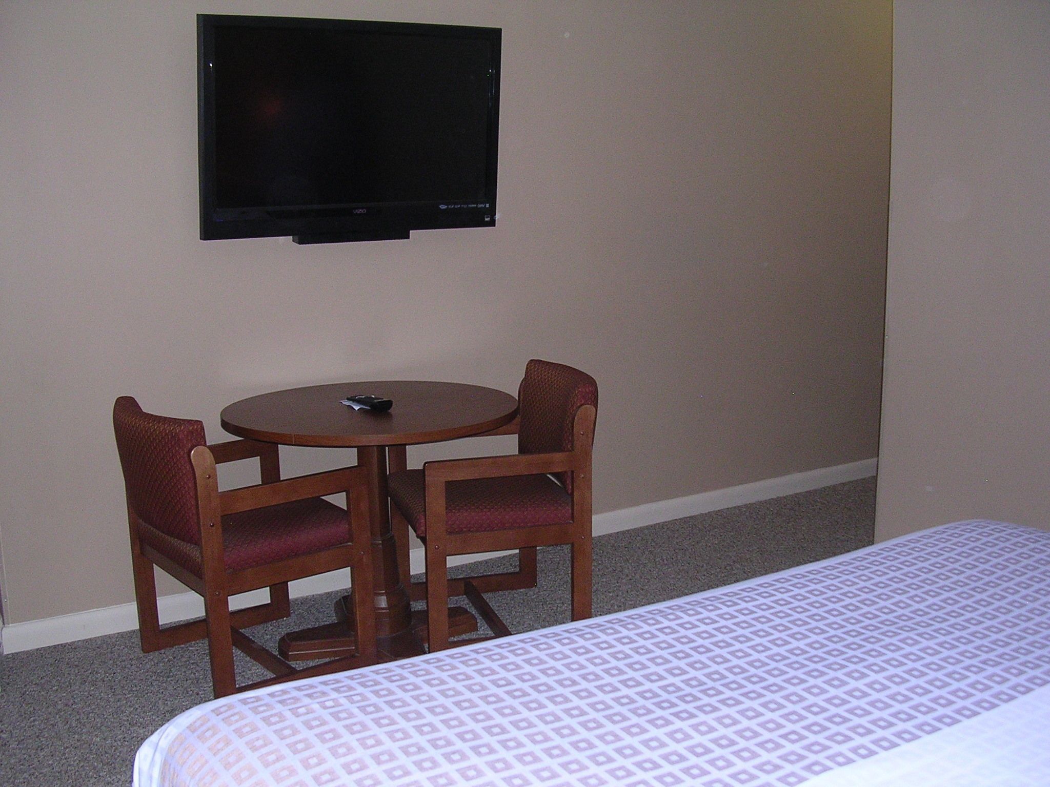 Una habitación de hotel con una cama, un televisor montado en la pared y una pequeña mesa redonda con dos sillas.