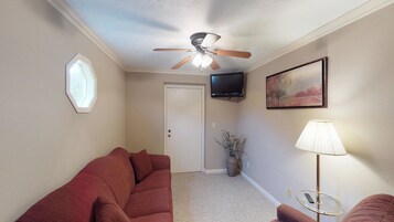 A living room with a ceiling fan, a television, a painting, a lamp, and a window.
