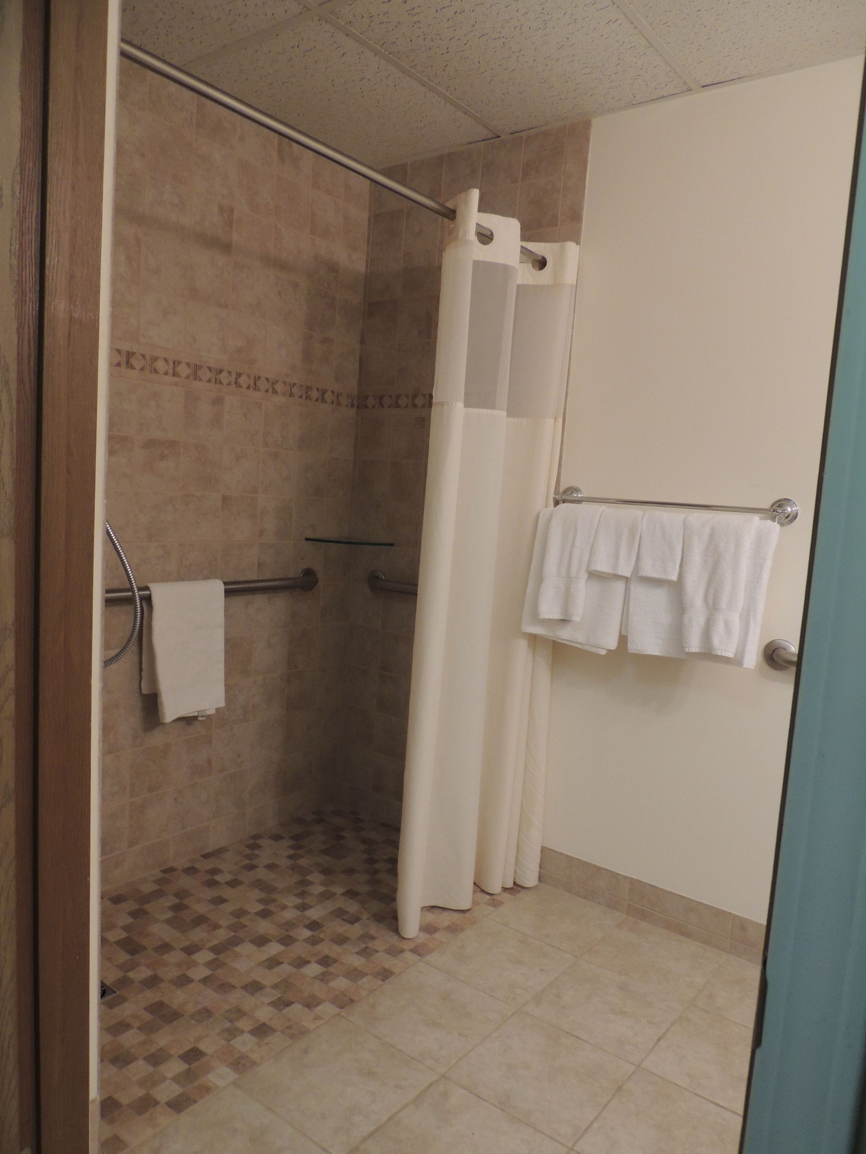 A shower area with a glass door, a towel rack with multiple towels, and a patterned floor.