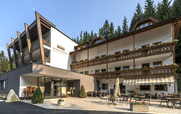 A hotel with a modern facade, outdoor seating area, and balconies with flower boxes. - Rechenmachers Rosengarten (Nova Levante)