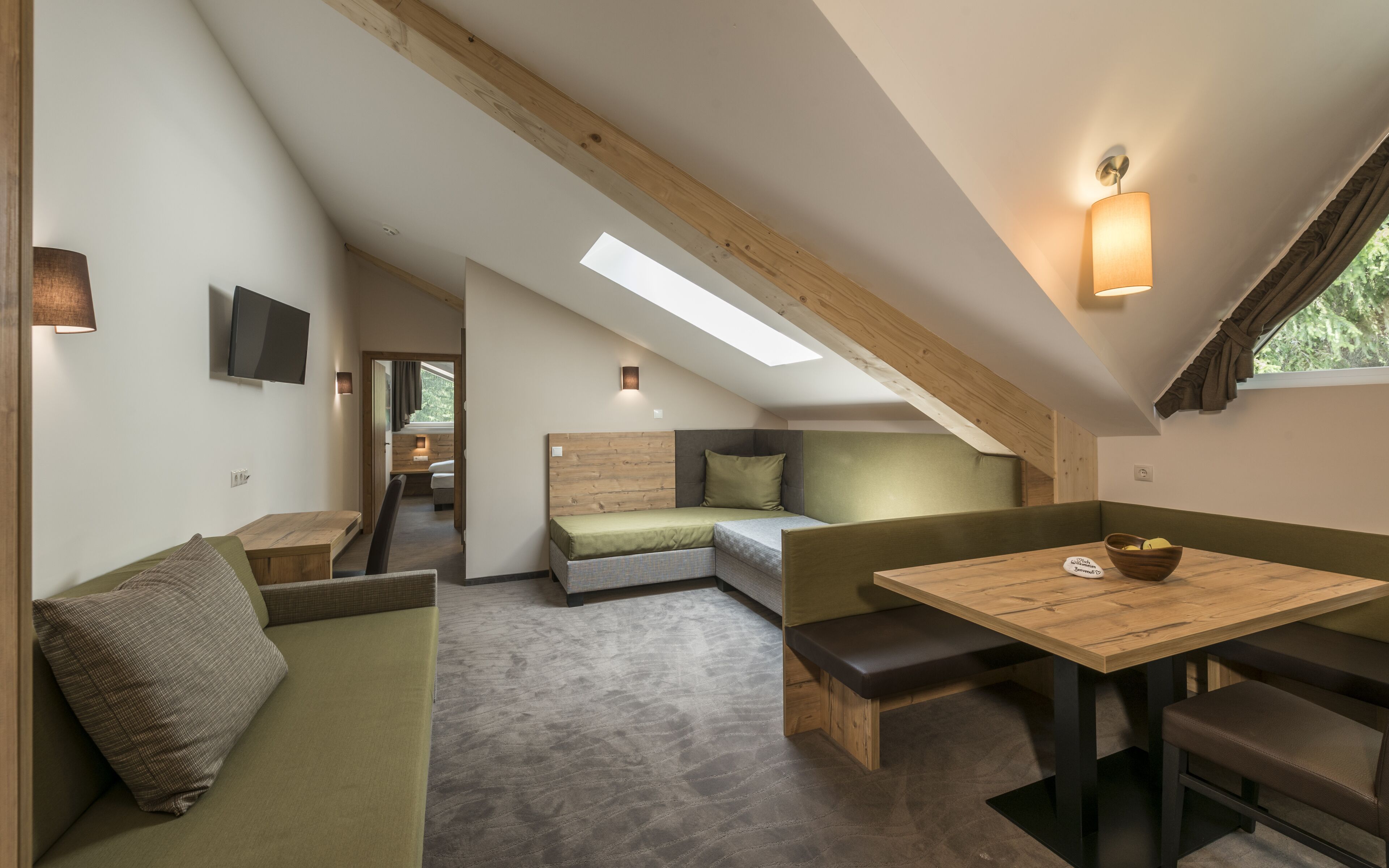 Une chambre de style loft, à la fois compacte et moderne, avec un plafond en pente, des sièges intégrés, un petit coin repas et un téléviseur fixé au mur.