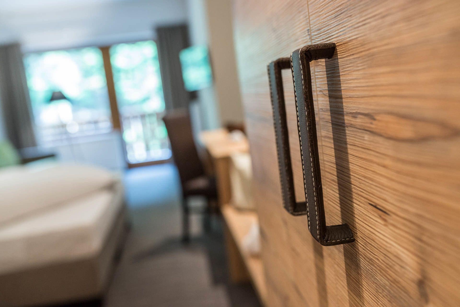 A wooden wardrobe with a black handle, a bed, and a chair in a hotel room.