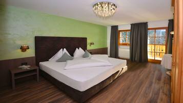 Habitación de hotel con una cama grande, suelo de madera, candelabro, mesita de noche y vistas al exterior a través de una ventana.