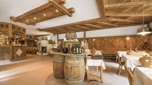 A rustic interior with wooden beams, a bar area with barrels, and tables set for dining. - Rechenmachers Rosengarten (Nova Levante)