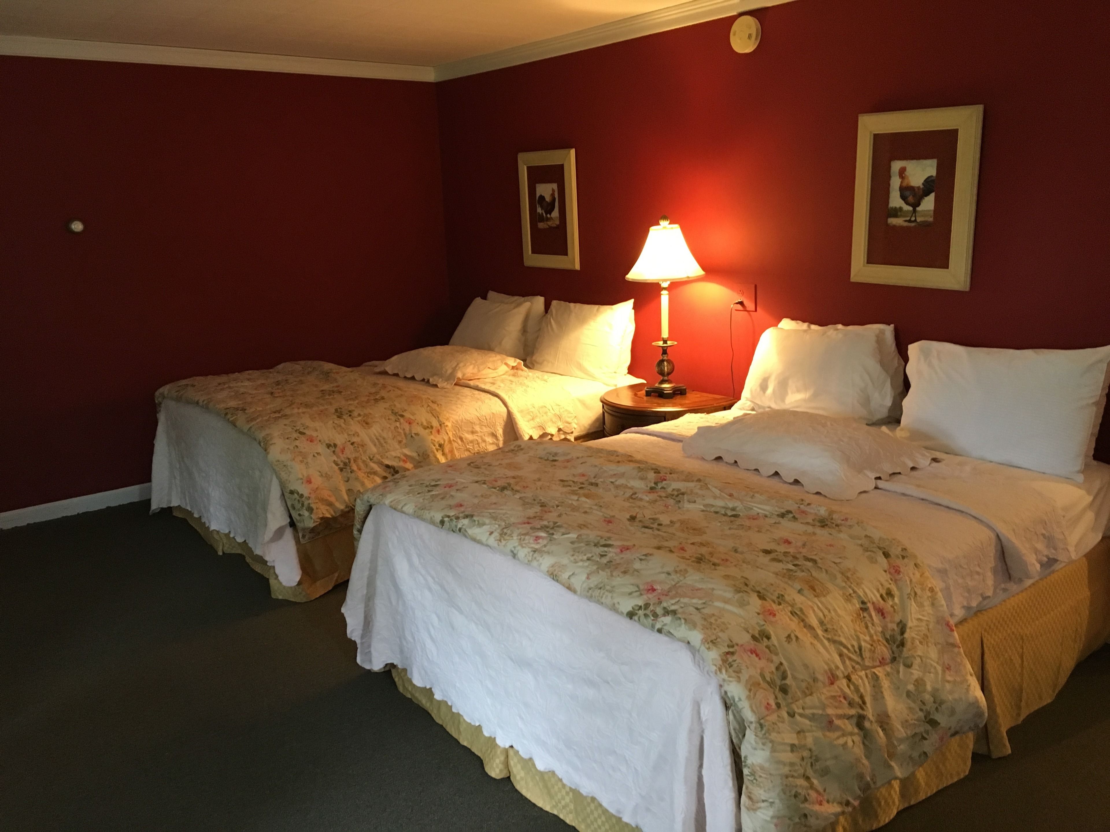 Una habitación de hotel con dos camas, una mesita de noche con lámpara y dos cuadros en la pared.
