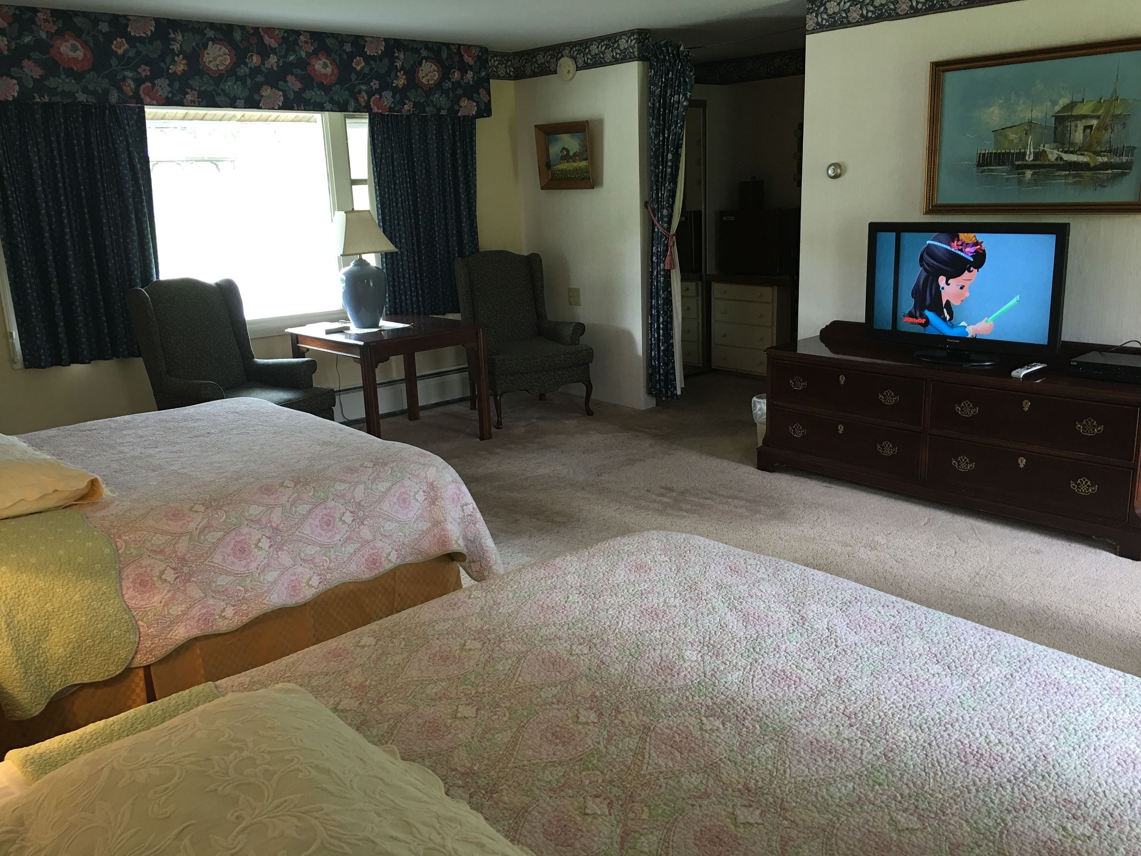 A hotel room with two beds, a television, a dresser, and a chair.