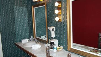 Un baño con tocador, espejo con luces, secador de pelo y pared roja.