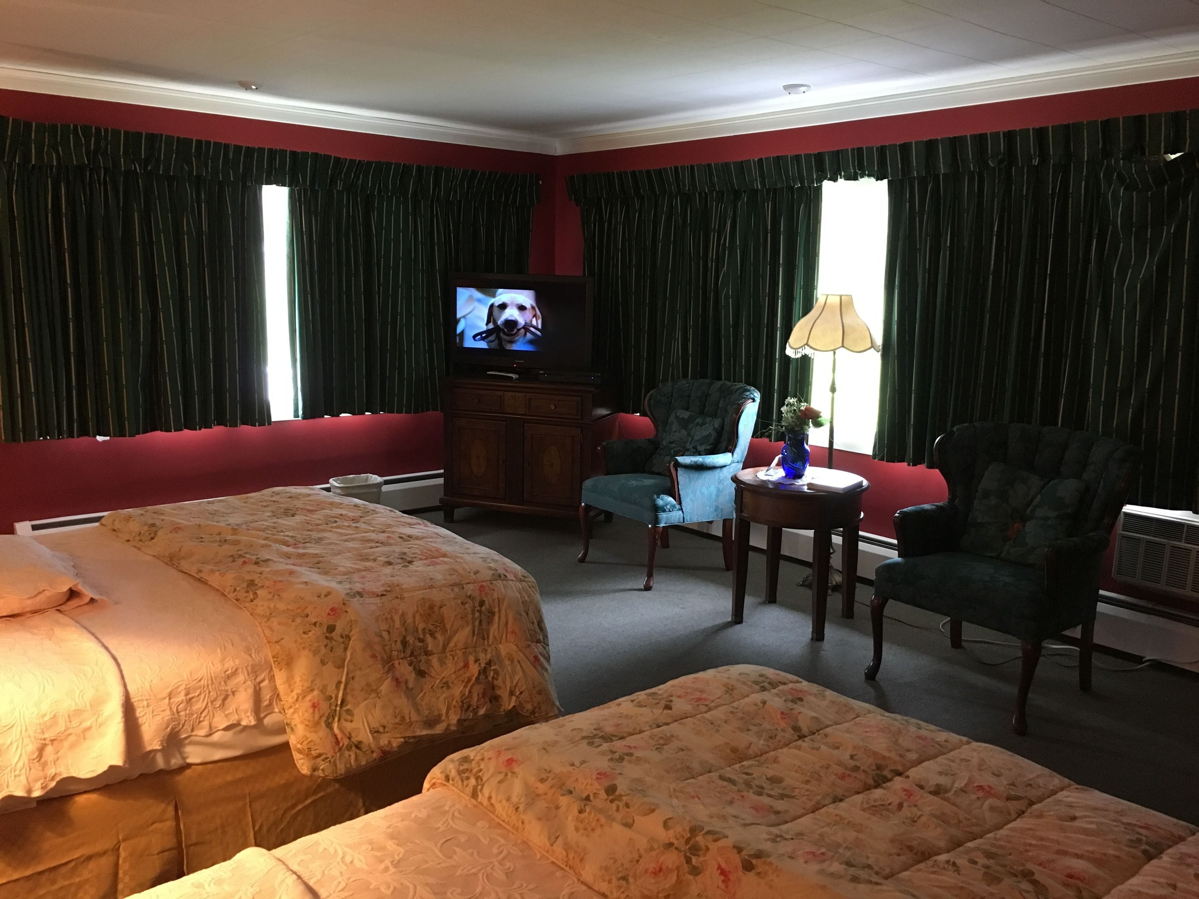 Quarto de hotel com duas camas, televisão, cadeira, mesa e abajur.