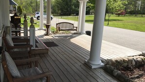 A covered porch with wooden benches and a swing, white columns, and a view of a street and greenery.