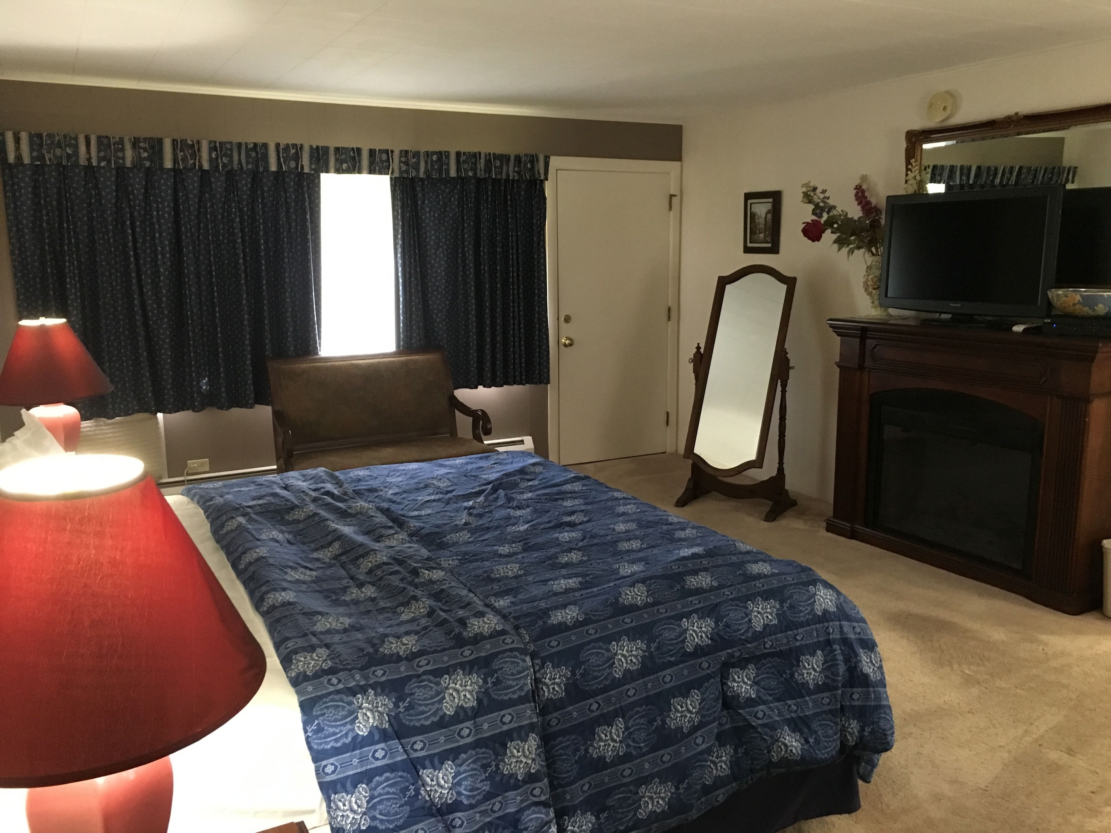 A hotel room with a bed, a chair, a television, a mirror, and a fireplace.