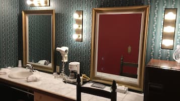A bathroom with two mirrors, a hairdryer, and a coffee maker on the counter.