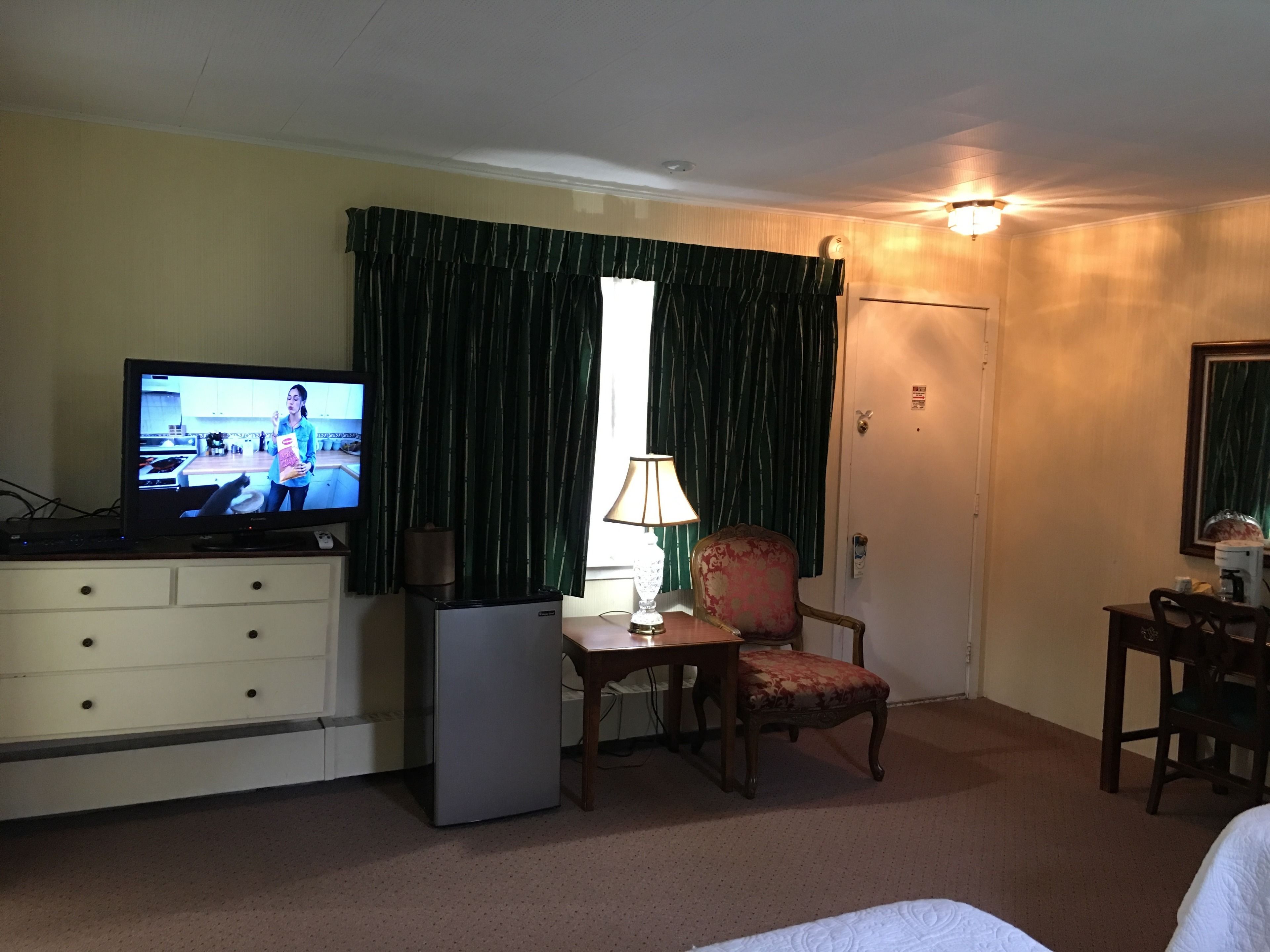 Una camera d'albergo con televisore, una scrivania con lampada, una sedia e un letto.