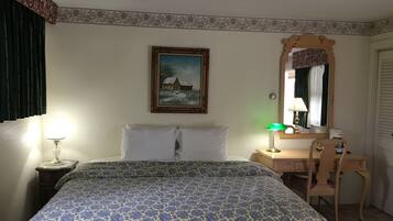 A hotel room with a bed, a desk, a chair, a lamp, a painting, and a mirror.