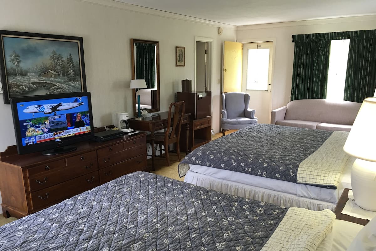A hotel room with two beds, a TV, a desk, a chair, and a painting on the wall.