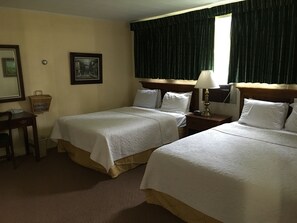 A hotel room with two beds, a nightstand with a lamp, a small table with a basket, and a framed picture on the wall.