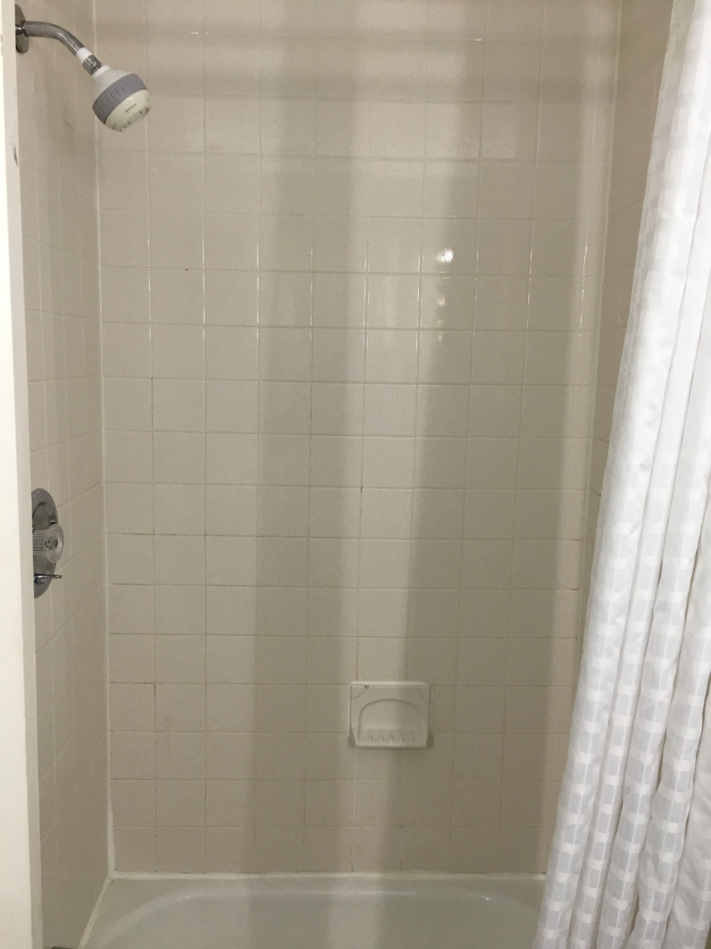 A shower area with a handheld showerhead, a small shelf, and a shower curtain.