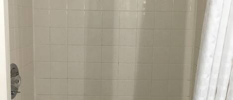 A shower area with a handheld showerhead, a small shelf, and a shower curtain.
