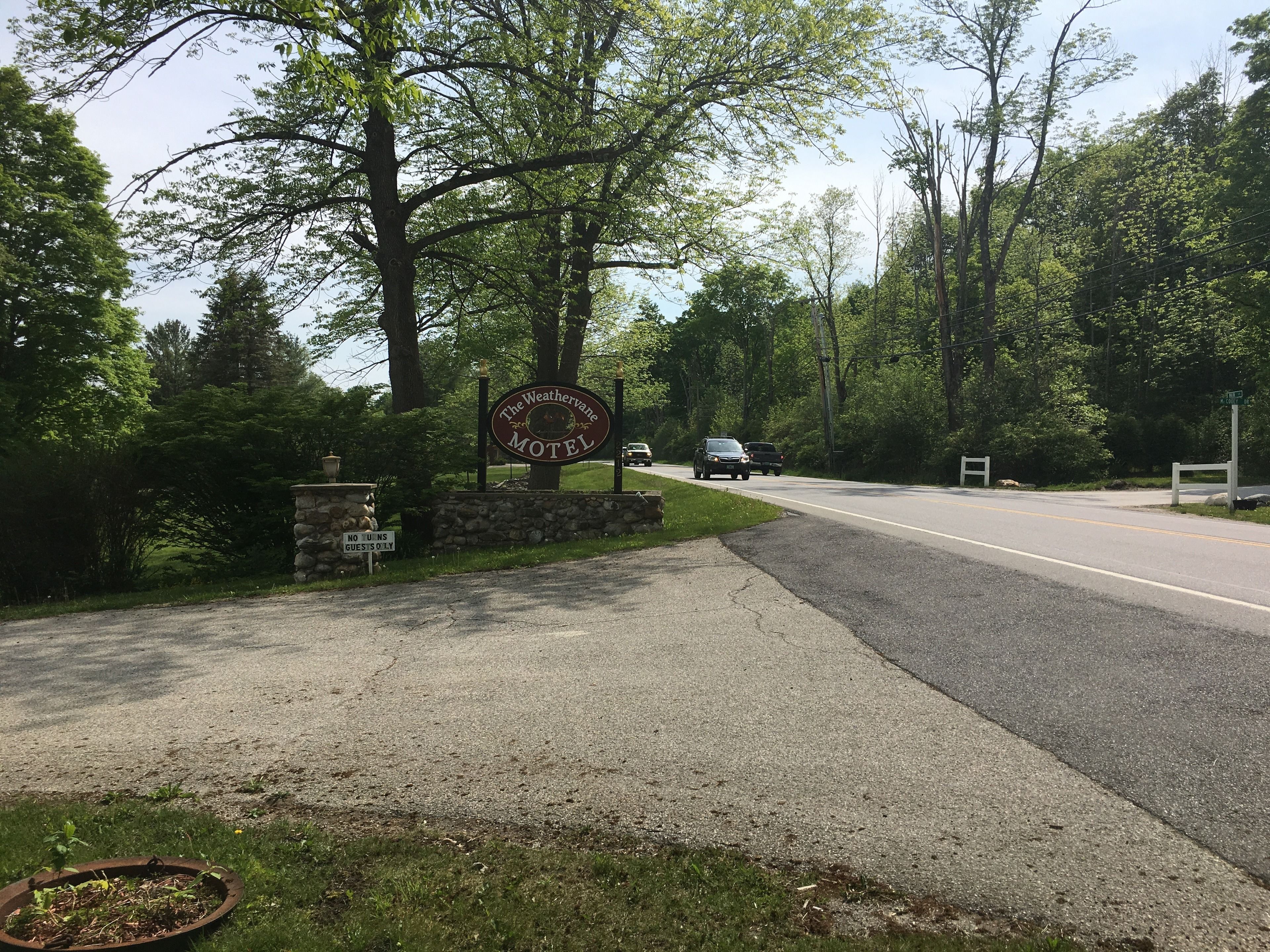 A motel sign with a stone wall and a road leading to it.